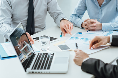 Businesspeople gathered around a laptop, examining financial graphs to determine the next steps for their company.