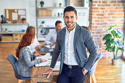 A manager smiles, leaning on a table at which his team is working.